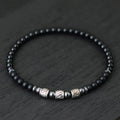 Black beaded bracelet with silver and gold accents on a dark wooden surface
