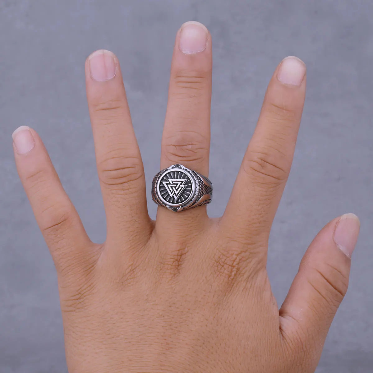 Hand wearing a silver ring with a black symbol on a gray background