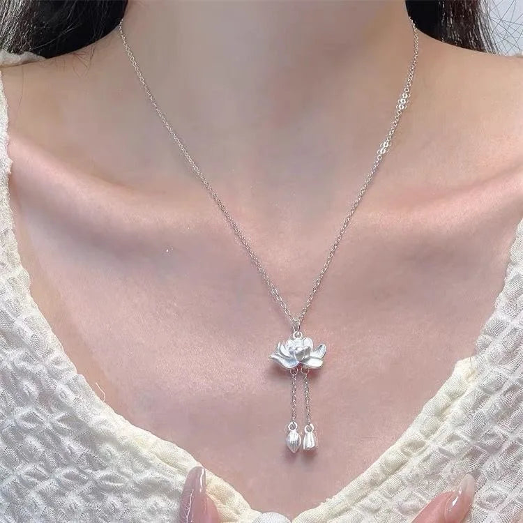 Silver necklace with a floral pendant worn by a person in a white textured garment.