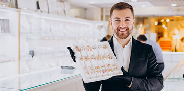 Man holding a display case of earrings in an elegant store setting